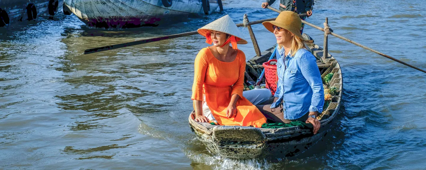 Three people in a boat that's being rowed through a floating river market
