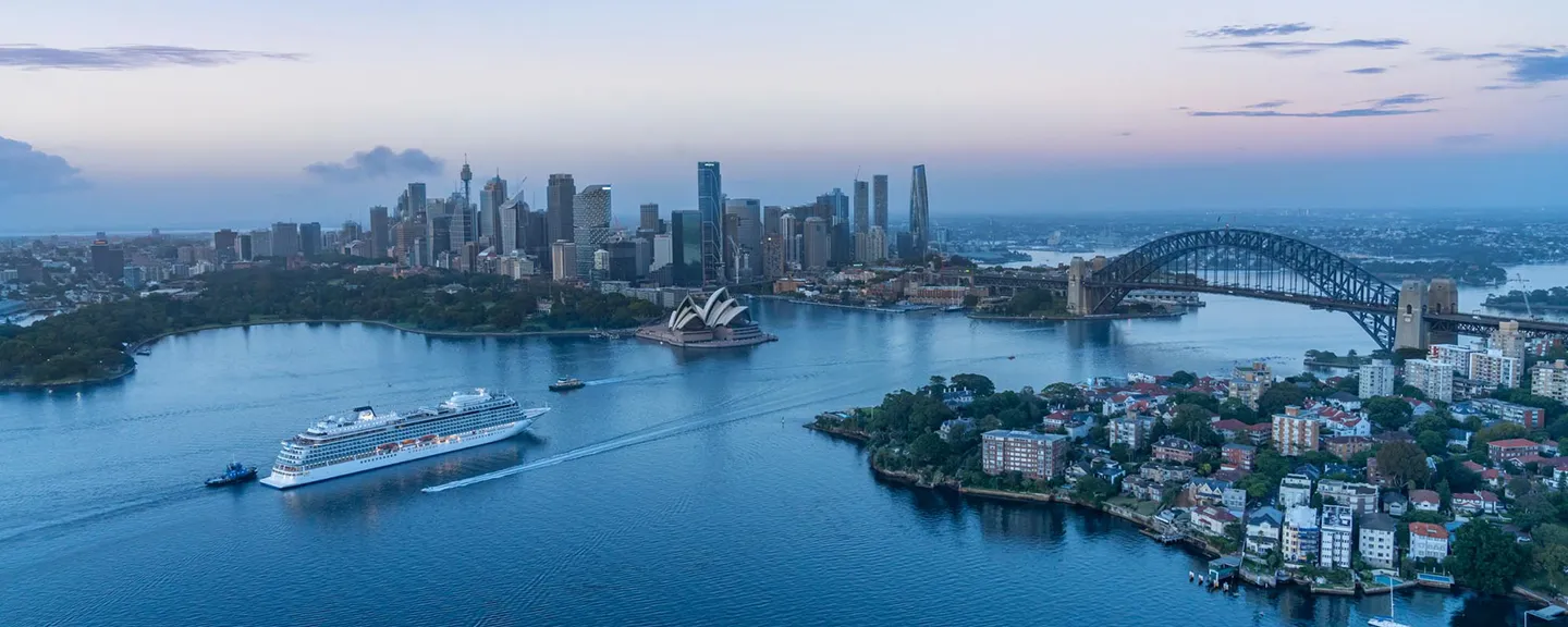 An ocean cruise ship sailing in a harbour with a cityscape in the background