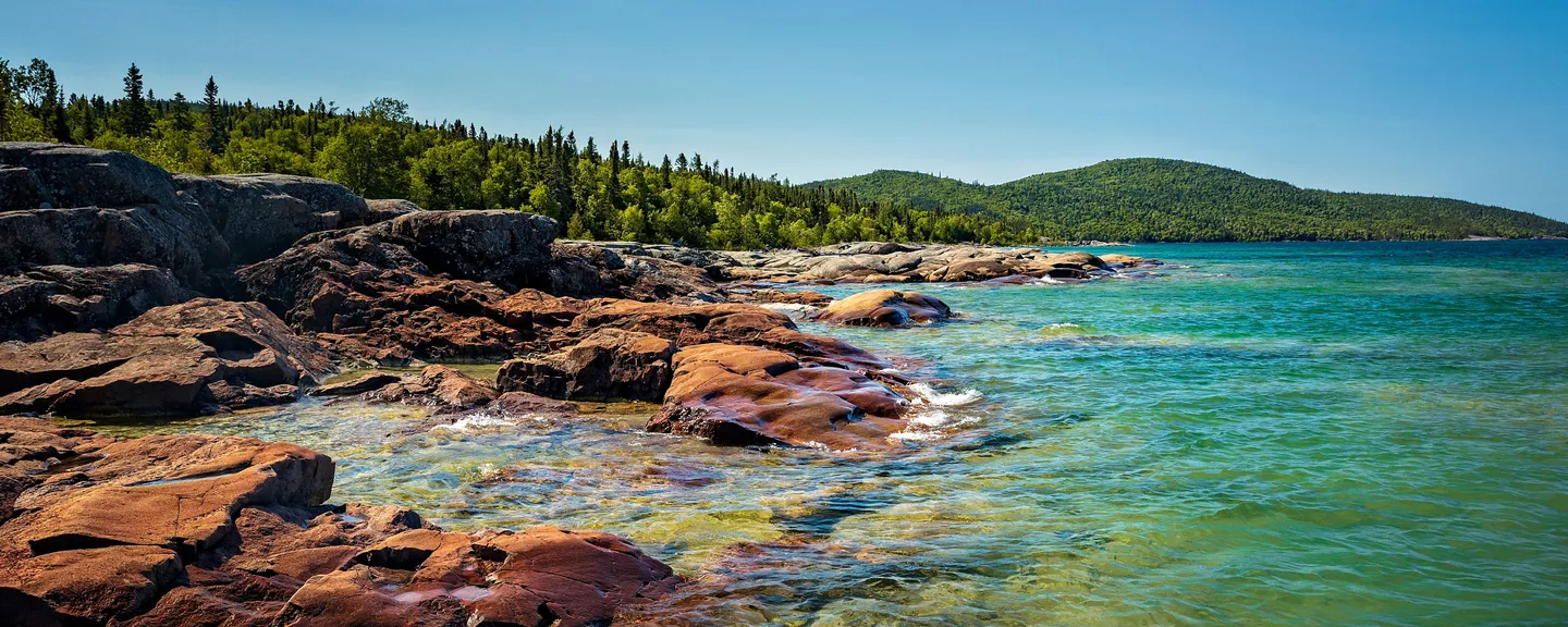 A rocky lakeside shore with forested hills in the background