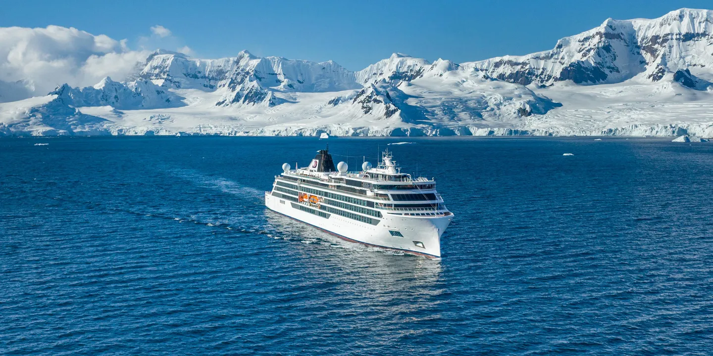 A cruise ship sailing on the ocean with a snowy coastline in the background