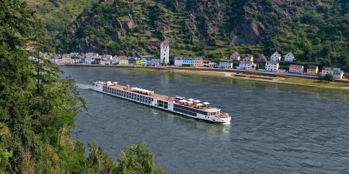 A river cruise ship sailing on a river with houses and hillsides in the background